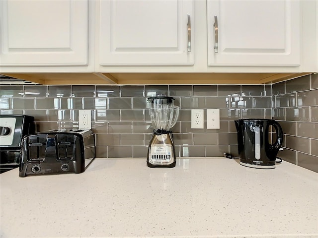 room details with tasteful backsplash, light stone countertops, and white cabinets