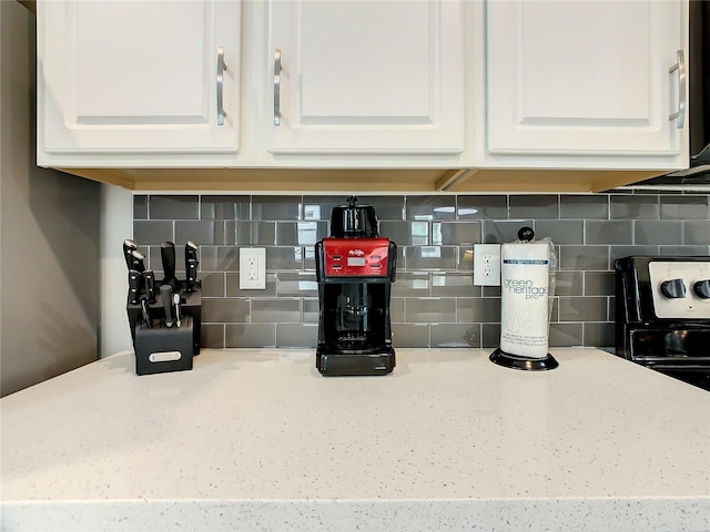 interior details featuring decorative backsplash, white cabinets, and light stone counters