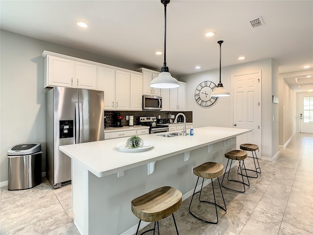 kitchen with tasteful backsplash, an island with sink, sink, pendant lighting, and stainless steel appliances