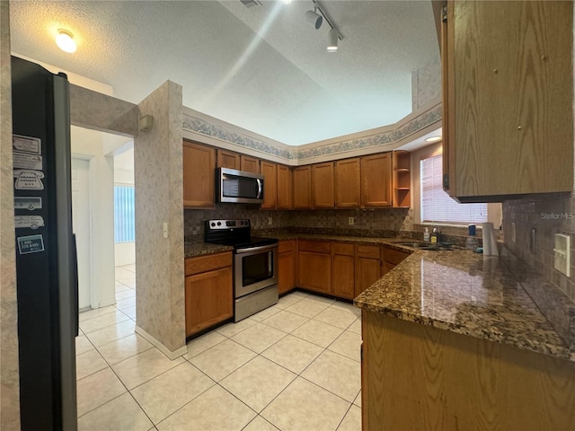 kitchen featuring a textured ceiling, dark stone countertops, stainless steel appliances, and light tile patterned floors