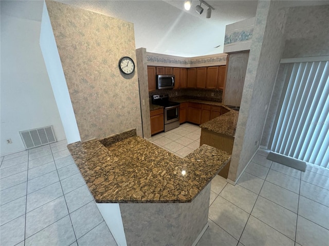 kitchen featuring dark stone countertops, appliances with stainless steel finishes, light tile patterned flooring, and kitchen peninsula