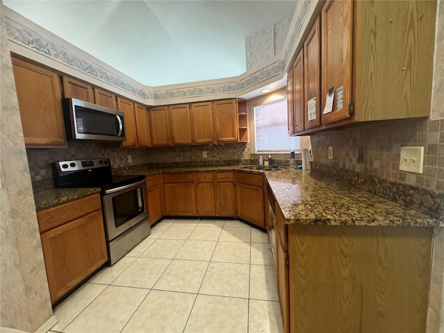 kitchen with dark stone countertops, stainless steel appliances, light tile patterned flooring, and sink