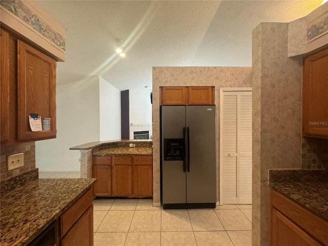 kitchen with stainless steel refrigerator with ice dispenser, a textured ceiling, light tile patterned floors, and dark stone countertops