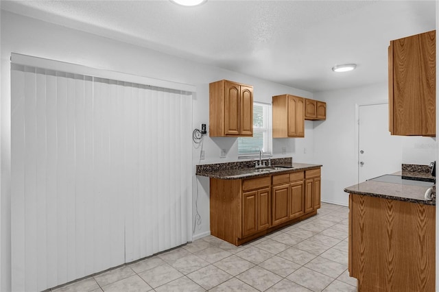 kitchen featuring a textured ceiling, dark stone countertops, sink, and light tile patterned floors