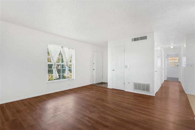 empty room with a textured ceiling, a wealth of natural light, and dark hardwood / wood-style floors