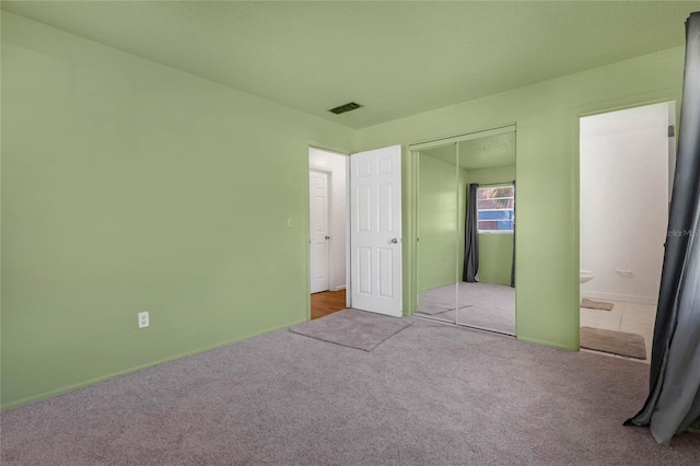 unfurnished bedroom featuring connected bathroom, light colored carpet, and a closet