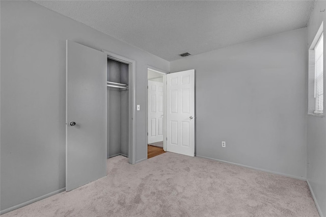 unfurnished bedroom featuring a closet, a textured ceiling, and light colored carpet