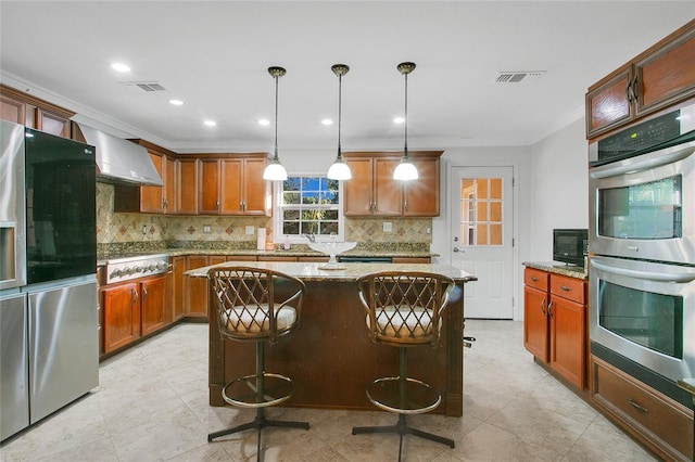 kitchen featuring stainless steel appliances, a kitchen island, decorative light fixtures, light stone countertops, and wall chimney exhaust hood