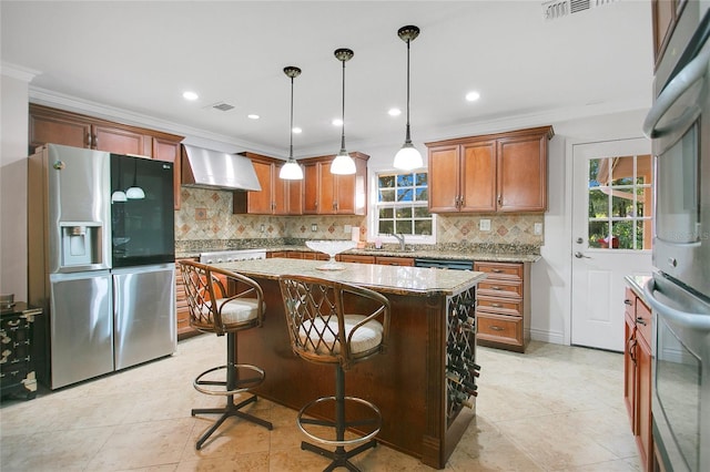 kitchen featuring appliances with stainless steel finishes, hanging light fixtures, decorative backsplash, wall chimney exhaust hood, and a center island