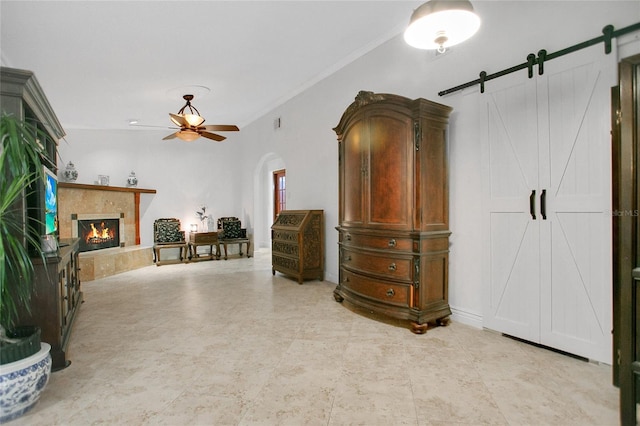 interior space with ornamental molding, a tiled fireplace, a barn door, and ceiling fan