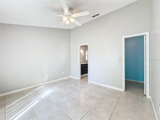 unfurnished bedroom featuring ensuite bath, ceiling fan, a textured ceiling, a walk in closet, and light tile patterned flooring