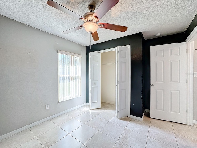 unfurnished bedroom featuring ceiling fan, a closet, light tile patterned floors, and a textured ceiling