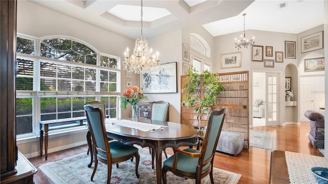 dining room featuring coffered ceiling, wood-type flooring, an inviting chandelier, and a high ceiling