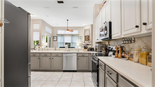 kitchen featuring gray cabinetry, tasteful backsplash, ceiling fan, stainless steel appliances, and light tile patterned floors