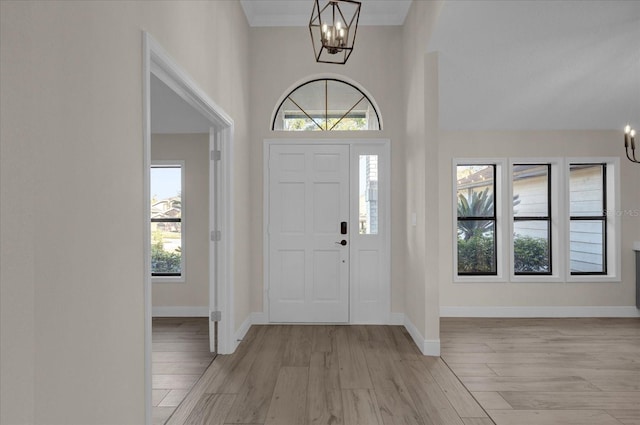 foyer entrance featuring ornamental molding, a wealth of natural light, light wood-type flooring, and an inviting chandelier