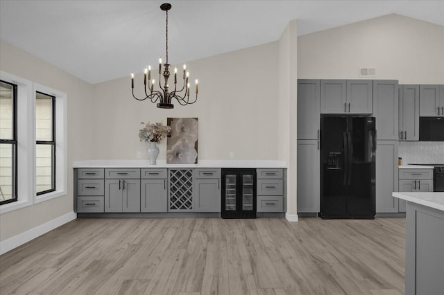 kitchen with lofted ceiling, wine cooler, gray cabinetry, and black fridge