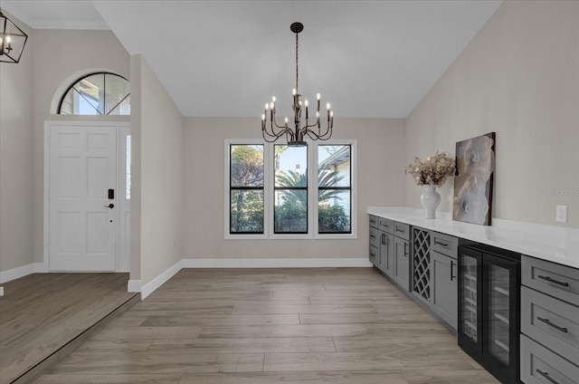 entryway featuring wine cooler, a notable chandelier, vaulted ceiling, and light hardwood / wood-style floors