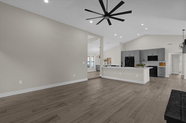 unfurnished living room with vaulted ceiling, light wood-type flooring, and ceiling fan with notable chandelier