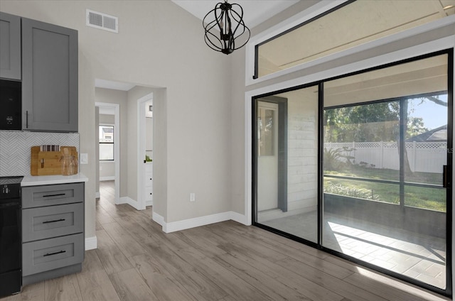 kitchen with hanging light fixtures, backsplash, a chandelier, light wood-type flooring, and gray cabinets