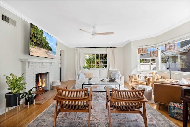 living room with hardwood / wood-style floors, a brick fireplace, ceiling fan, and ornamental molding