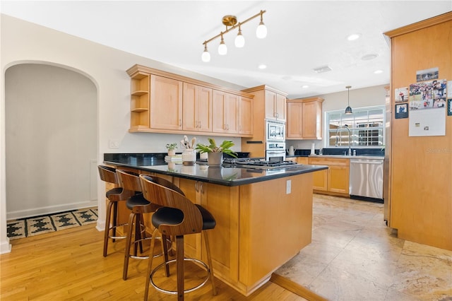 kitchen with kitchen peninsula, appliances with stainless steel finishes, a kitchen breakfast bar, light brown cabinetry, and light hardwood / wood-style floors