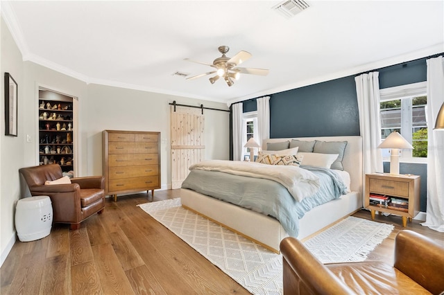 bedroom featuring a barn door, ceiling fan, crown molding, and hardwood / wood-style flooring