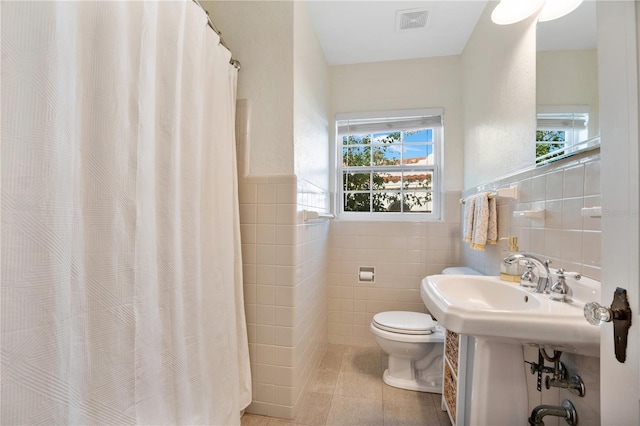 bathroom featuring tile patterned flooring, toilet, tile walls, and walk in shower