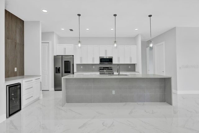 kitchen with appliances with stainless steel finishes, white cabinetry, beverage cooler, and a kitchen island with sink