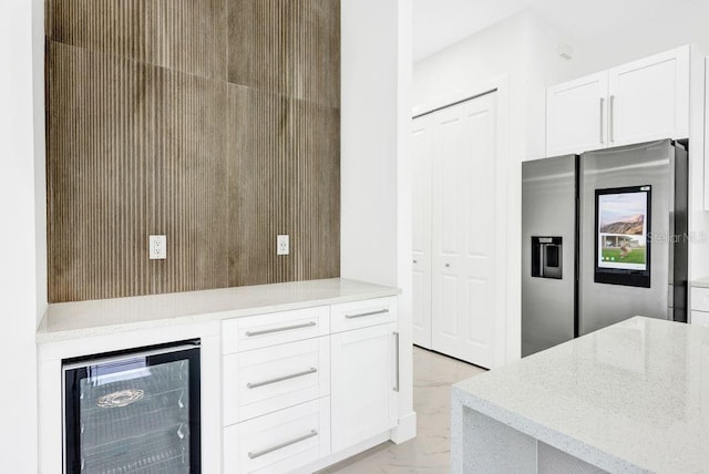 kitchen with white cabinetry, stainless steel fridge, beverage cooler, and light stone counters