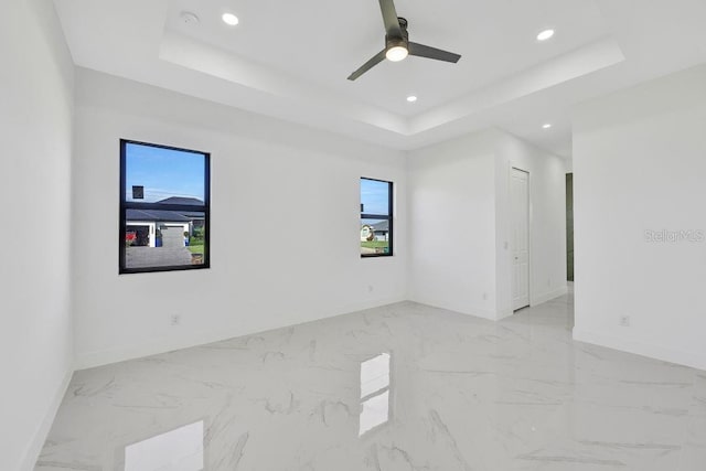 empty room featuring ceiling fan and a raised ceiling