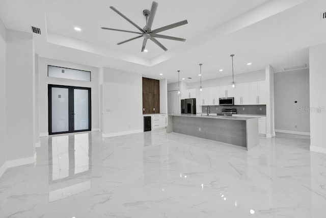 kitchen with ceiling fan, an island with sink, decorative light fixtures, white cabinets, and appliances with stainless steel finishes