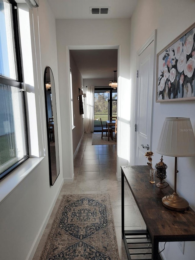 hallway with light tile patterned floors, an inviting chandelier, and plenty of natural light