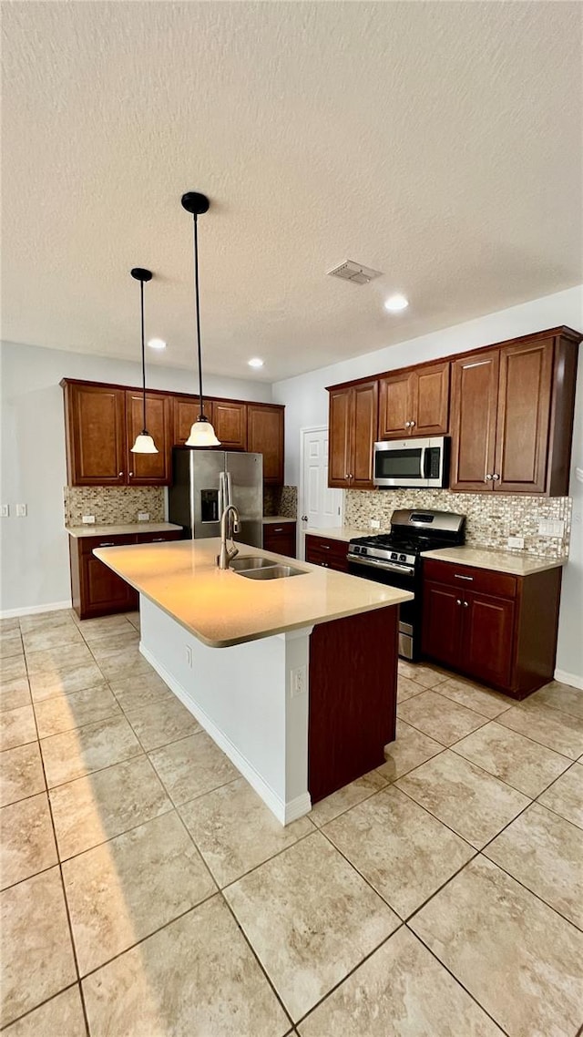 kitchen with tasteful backsplash, a textured ceiling, hanging light fixtures, stainless steel appliances, and a center island with sink