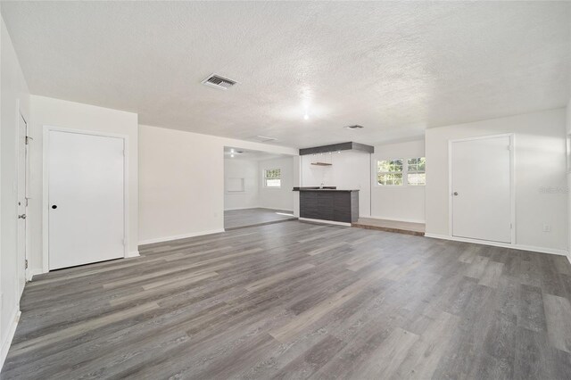 unfurnished living room with dark wood-type flooring, a textured ceiling, and bar area