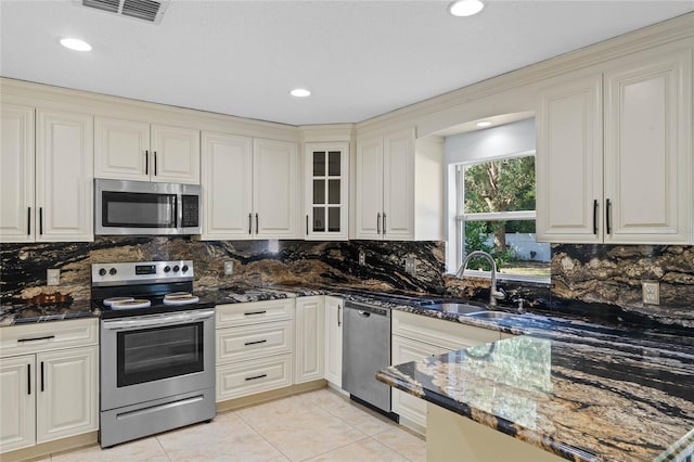 kitchen with appliances with stainless steel finishes, decorative backsplash, sink, and dark stone counters