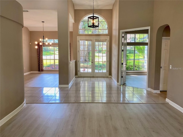 tiled entryway with french doors, a towering ceiling, and a notable chandelier