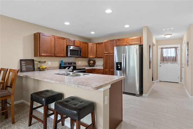 kitchen with sink, a breakfast bar, appliances with stainless steel finishes, and kitchen peninsula