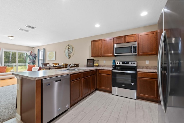 kitchen with light wood-type flooring, stainless steel appliances, sink, and kitchen peninsula