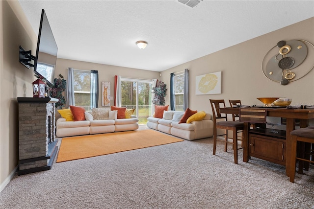 living room featuring a textured ceiling, a stone fireplace, carpet floors, and plenty of natural light