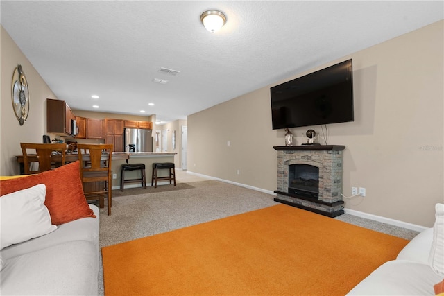 carpeted living room with a stone fireplace and a textured ceiling