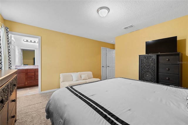 bedroom with light carpet, a textured ceiling, and ensuite bath