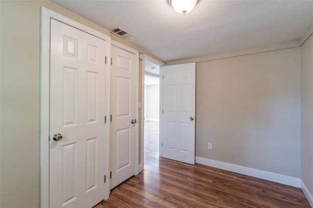 unfurnished bedroom with a textured ceiling and dark hardwood / wood-style flooring