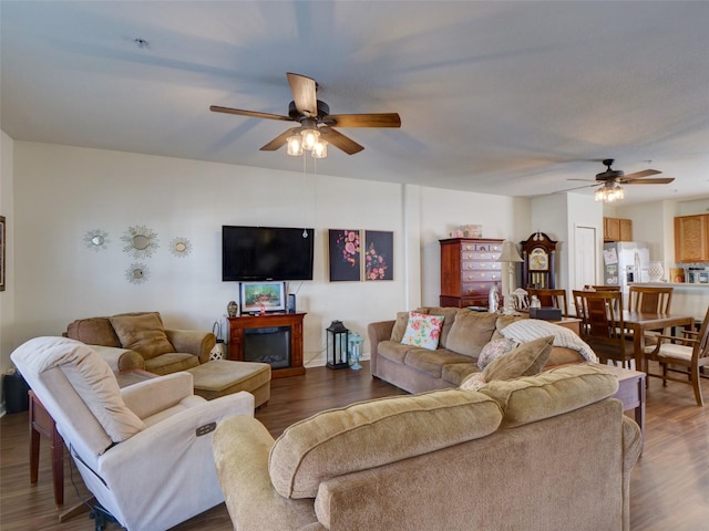 living area with a glass covered fireplace, ceiling fan, and wood finished floors