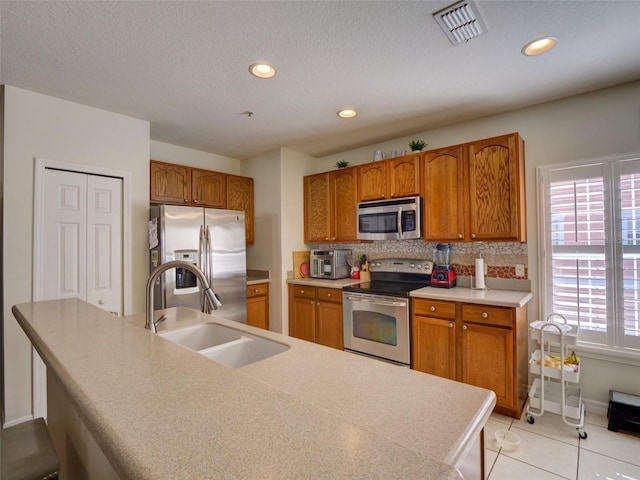 kitchen featuring brown cabinetry, visible vents, stainless steel appliances, and a sink