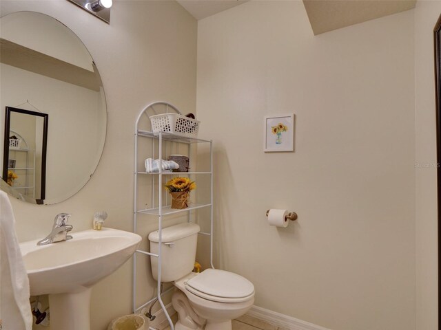 half bathroom with toilet, baseboards, a sink, and tile patterned floors