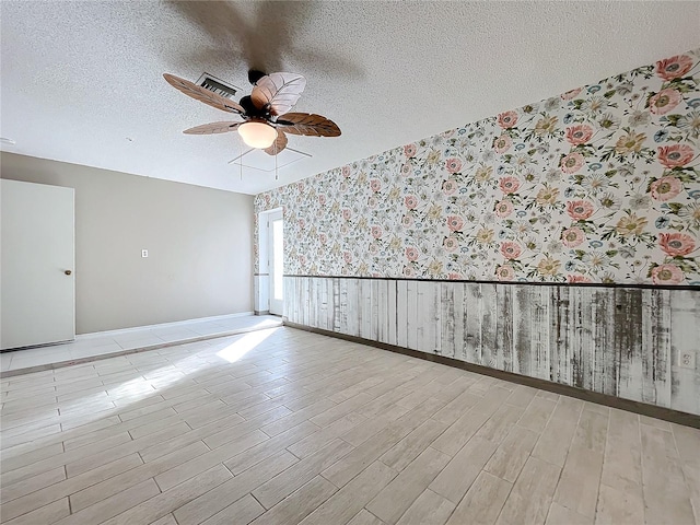 unfurnished room with light hardwood / wood-style floors, a textured ceiling, wooden walls, and ceiling fan