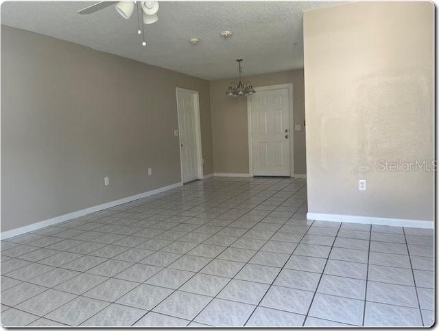 unfurnished room with a textured ceiling, ceiling fan with notable chandelier, and light tile patterned floors