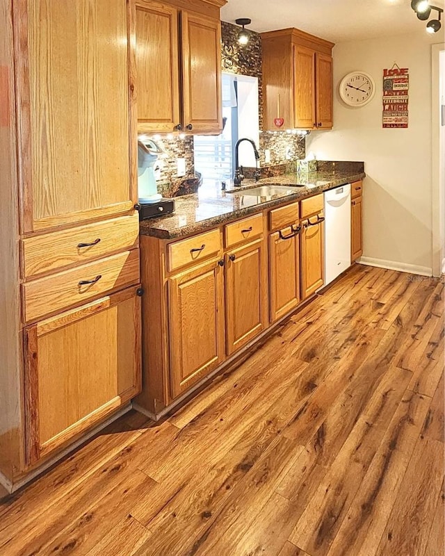 kitchen featuring backsplash, dark stone counters, white dishwasher, sink, and light hardwood / wood-style flooring