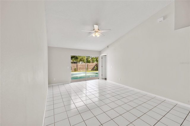 empty room with vaulted ceiling, light tile patterned floors, baseboards, and ceiling fan