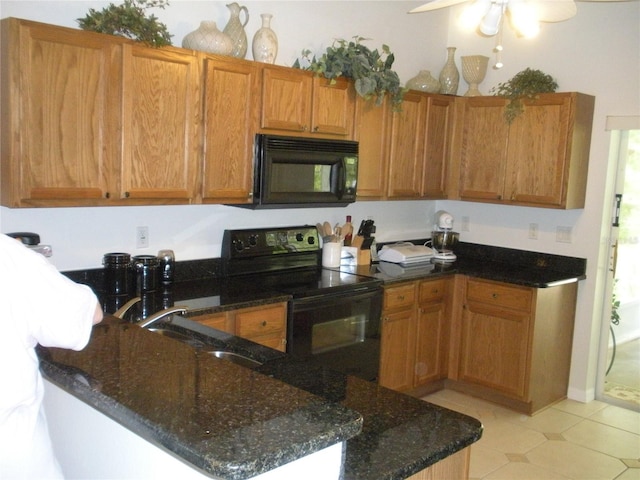 kitchen with black appliances, kitchen peninsula, ceiling fan, dark stone countertops, and light tile patterned floors